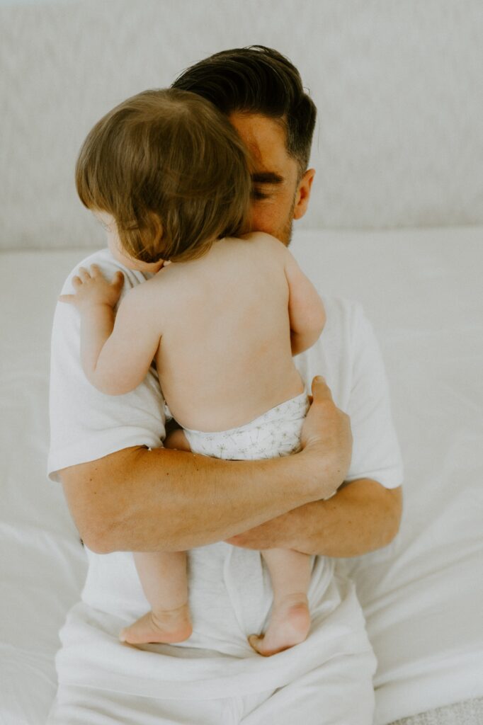 Vater hält sein Baby in der Windel im Arm vor hellem Hintergrund